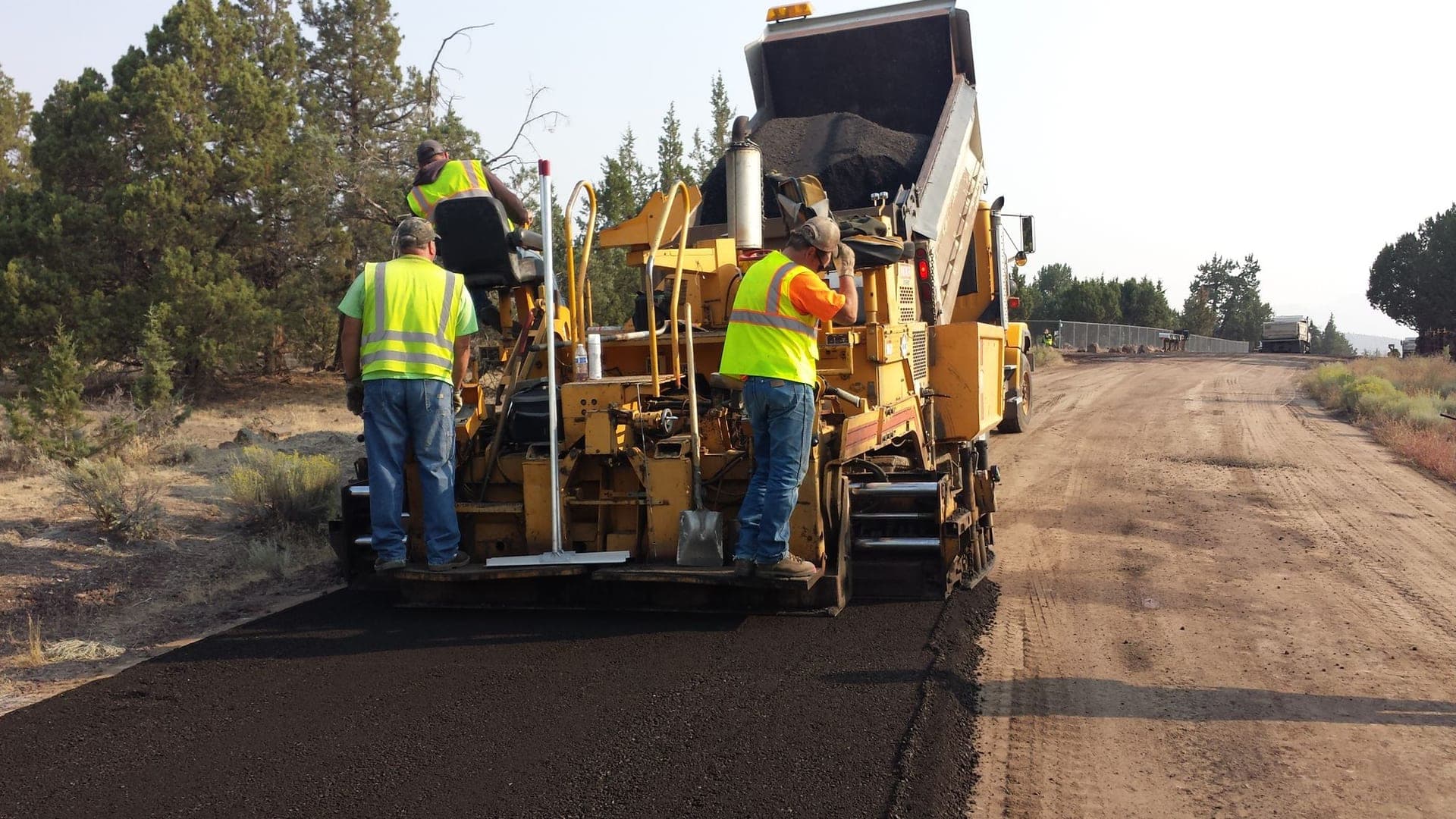 Paving crew laying hot-mix asphalt behind a paver on a two-lane road