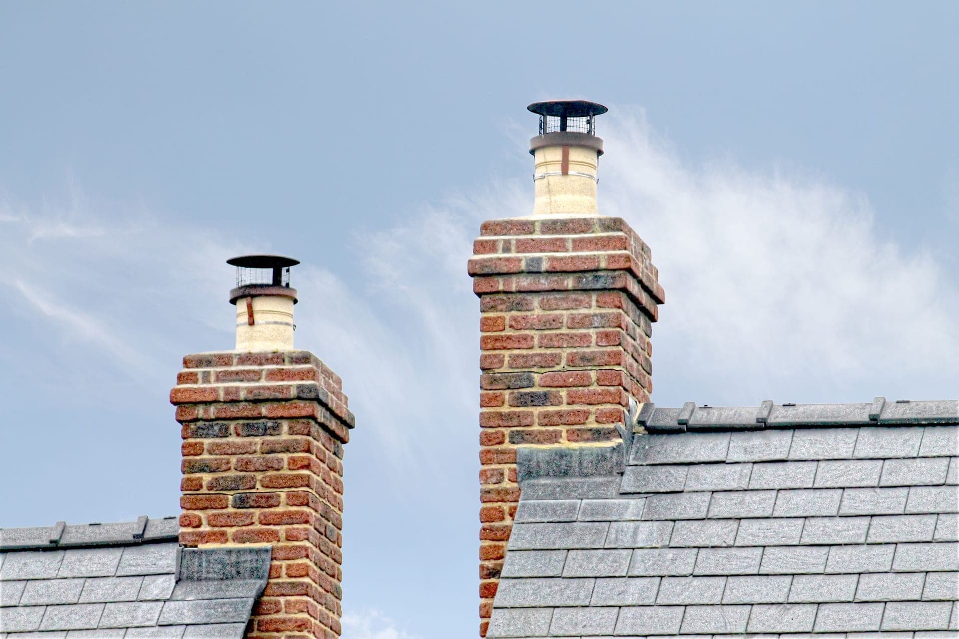 Brick chimneys with caps on a slate roof against a blue sky
