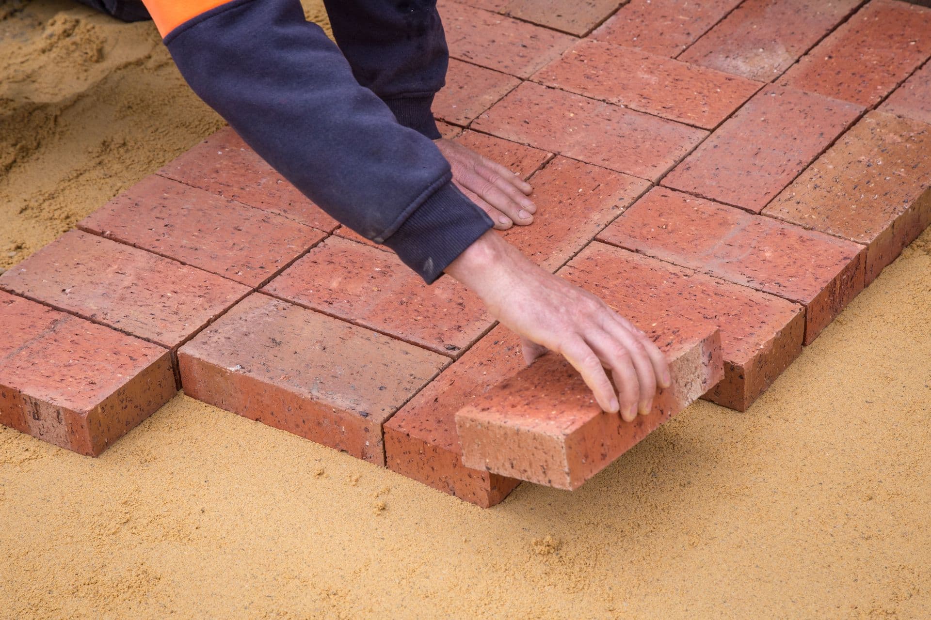 Worker pressing clay pavers into a screeded sand bed by hand