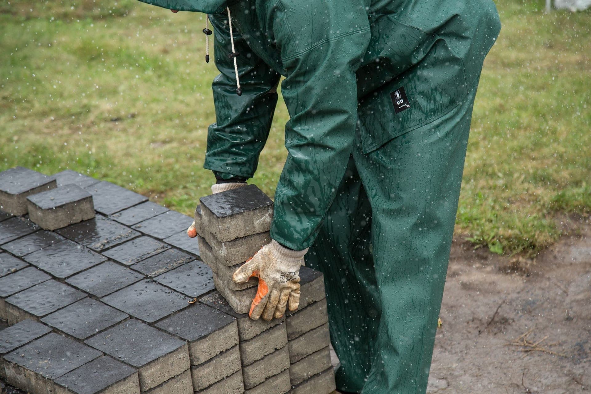 Worker in rain gear unloading concrete pavers from a stack
